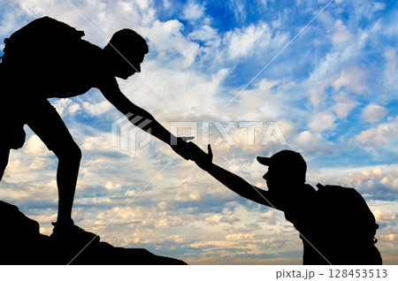 Silhouette of a male mountaineer giving a helping hand to his partner Silhouette of a male mountaineer giving a helping hand to his partner 128453513