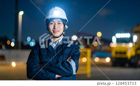 夜に腕組みをして建設現場に立つヘルメットを被り作業服を着た監督 128453713
