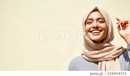 Smiling woman with a beige hijab in front of a neutral background 128454331