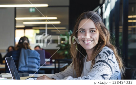 A young woman smiles while working on a laptop in a cozy workspace 128454332