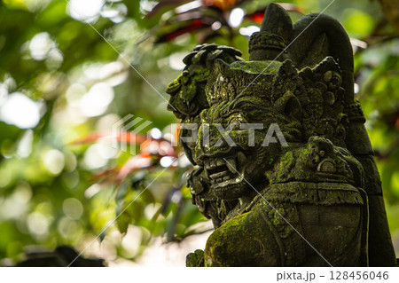 Monkey sculpture fully covered with green moss in Ubud's Monkey Forest. Bali, Indonesia. 128456046