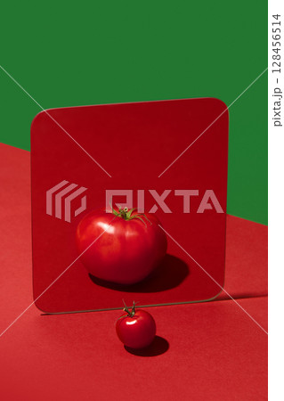 Small cherry tomato reflects as large tomato in square mirror on red background Small cherry tomato reflects as large tomato in square mirror on red background 128456514