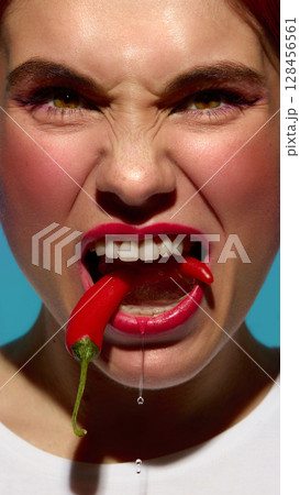 Aggressive woman biting red chili frozen in ice with tense facial expression and dripping water Aggressive woman biting red chili frozen in ice with tense facial expression and dripping water 128456561