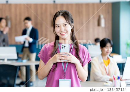 オフィスでスマホを使う若いビジネスウーマン オフィスでスマホを使う若いビジネスウーマン 128457124