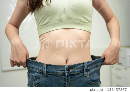 Young Asian woman losing weight wearing loose pants in oversize jeans. 128457877