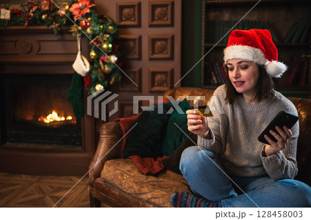 Merry Christmas. Young woman shopping online holding smartphone paying with gold credit card for Christmas gifts. Girl buying on Internet enter credit card details enjoying winter holidays at home Merry Christmas. Young woman shopping online holding smartphone paying with gold credit card for Christmas gifts. Girl buying on Internet enter credit card details enjoying winter holidays at home 128458003