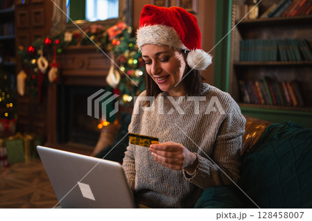 Merry Christmas. Young woman shopping online with laptop paying with gold credit card for Christmas gifts. Girl buying on Internet enter credit card details enjoying winter holidays at home Merry Christmas. Young woman shopping online with laptop paying with gold credit card for Christmas gifts. Girl buying on Internet enter credit card details enjoying winter holidays at home 128458007