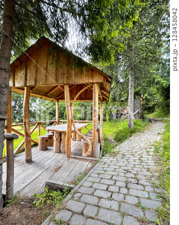 Wooden gazebo in forest with stone path and lush greenery. 128458042