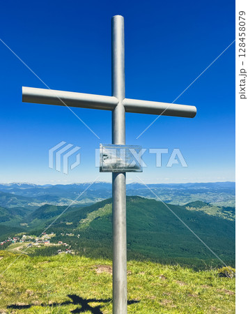 Metal cross on mountain summit with panoramic view and blue sky 128458079