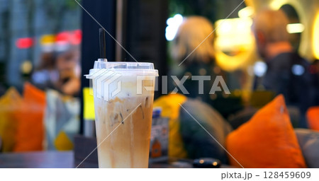 Relaxed young professional sipping chilled coffee with creamy topping at sunlit sidewalk cafe, capturing casual urban lifestyle moment 128459609