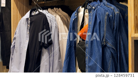 Multiple shots showcasing various shirts, a denim jacket, and a black bag hanging in a wooden wardrobe, creating a stylish and organized fashion display. Concept fashion clothes Multiple shots showcasing various shirts, a denim jacket, and a black bag hanging in a wooden wardrobe, creating a stylish and organized fashion display. Concept fashion clothes 128459731