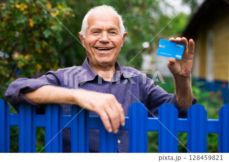 Old man with credit card standing beside his house Old man with credit card standing beside his house 128459821