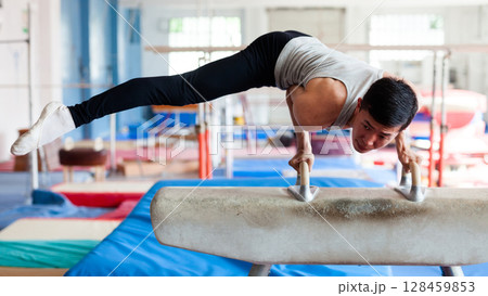 Young man performing gymnastic elements on pommel horse Young man performing gymnastic elements on pommel horse 128459853
