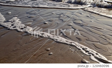 Ocean waves gently caress the sandy shore, creating mesmerizing patterns and textures as the water recedes, leaving behind a beautiful display of natural artistry 128460096