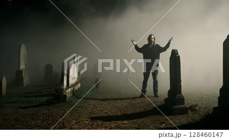 Solitary male figure standing with outstretched arms amid foggy cemetery, embodying haunting grief and supernatural contemplation during nocturnal hours 128460147