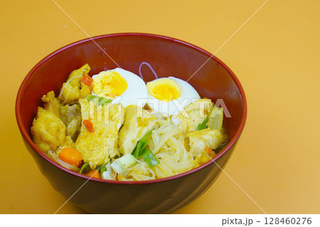 A vibrant bowl of Bihun Kari or Indonesian curry vermicelli noodles, chicken, eggs, and vegetables in a rich yellow broth. A vibrant bowl of Bihun Kari or Indonesian curry vermicelli noodles, chicken, eggs, and vegetables in a rich yellow broth. 128460276