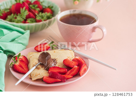 Crepes with chocolate spread and fresh strawberries, served with tea on pink background Crepes with chocolate spread and fresh strawberries, served with tea on pink background 128461753