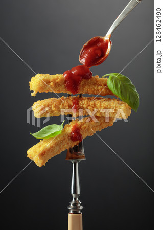 Fish fingers with basil and ketchup on a fork. Fish fingers with basil and ketchup on a fork. 128462490