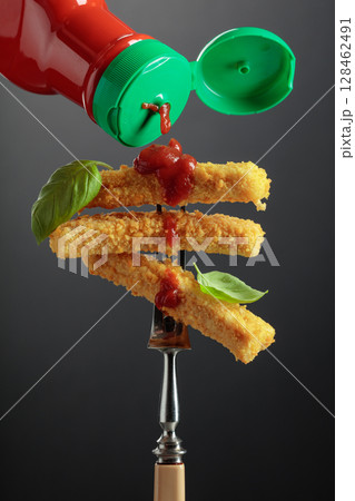 Fish fingers with basil and ketchup on a fork. Fish fingers with basil and ketchup on a fork. 128462491