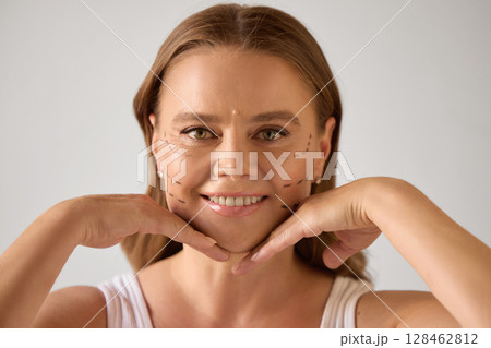 Anti-aging solutions. Mature woman with cosmetic surgery marks smiling and posing with hands near chin Anti-aging solutions. Mature woman with cosmetic surgery marks smiling and posing with hands near chin 128462812