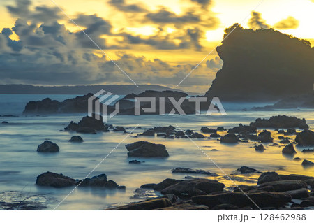A mystical long exposure shot of a rocky coastline at sunset, with a waterfall-like rock formation near Papuma Beach, Jember. East Java, Indonesia. A mystical long exposure shot of a rocky coastline at sunset, with a waterfall-like rock formation near Papuma Beach, Jember. East Java, Indonesia. 128462988