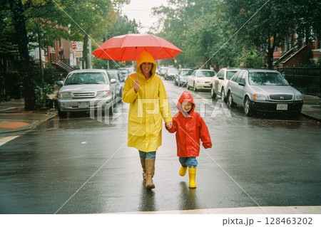 A woman and a child are walking down a street in the rain, holding hands A woman and a child are walking down a street in the rain, holding hands 128463202
