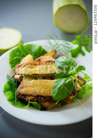 Fried zucchini slices with salad greens on a gray background Fried zucchini slices with salad greens on a gray background 128463500