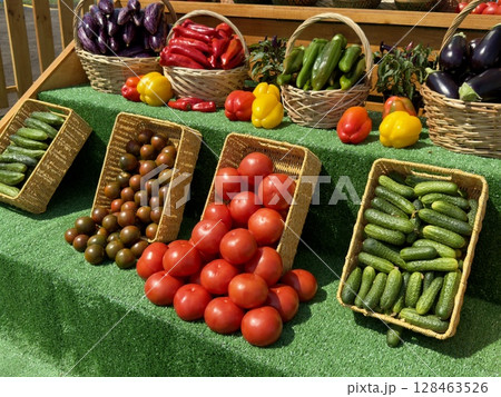 Red tomatoes, green cucumbers, black tomatoes, peppers, and eggplants are displayed in wicker baskets on a market stall, creating a colorful and inviting scene Red tomatoes, green cucumbers, black tomatoes, peppers, and eggplants are displayed in wicker baskets on a market stall, creating a colorful and inviting scene 128463526