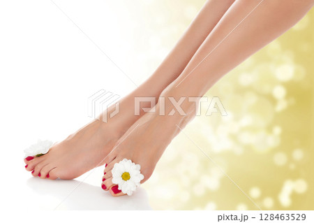 Beautiful female legs with daisy flower on golden blurred background. 128463529