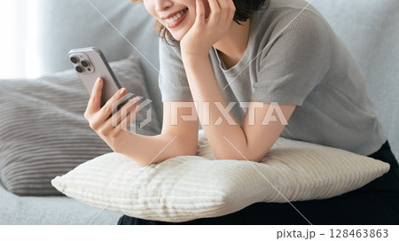 ソファに座ってスマートフォンを使う笑顔の女性 ソファに座ってスマートフォンを使う笑顔の女性 128463863