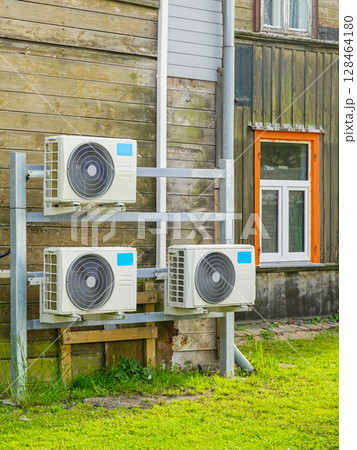 Multiple Air-to-Air Heat Pump Outdoor Units Installed on Wooden Wall of a Residential Building 128464180