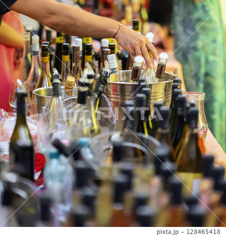 Hand reaching for wine bottle from metal ice bucket at festive wine tasting with many labels visible. Concept of wine selection, testing, celebration and premium alcohol 128465418