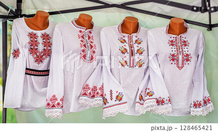 Bulgarian traditional embroidered shirts with colorful folk patterns on mannequins at outdoor market stall. Concept of embroidery, ethnic clothing and cultural heritage, craft textile Bulgarian traditional embroidered shirts with colorful folk patterns on mannequins at outdoor market stall. Concept of embroidery, ethnic clothing and cultural heritage, craft textile 128465421