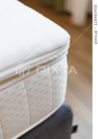 A close-up view of a soft, plush mattress topper resting atop a mattress in a modern bedroom. The warm wooden flooring and gentle light create a cozy atmosphere 128465438