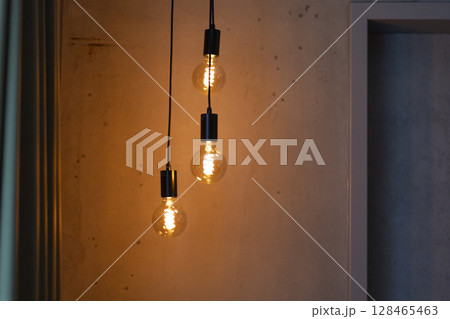 Three warm light bulbs hang from black cables, illuminating a textured wall in a contemporary room. The glow creates a cozy atmosphere, enhancing the space's design 128465463