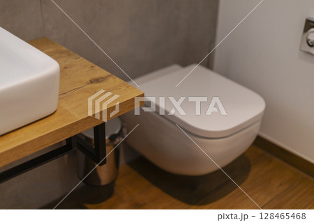 A clean and modern bathroom showcases a contemporary toilet beside a wooden countertop with a white sink. The space is bright and uncluttered, emphasizing simplicity and style 128465468