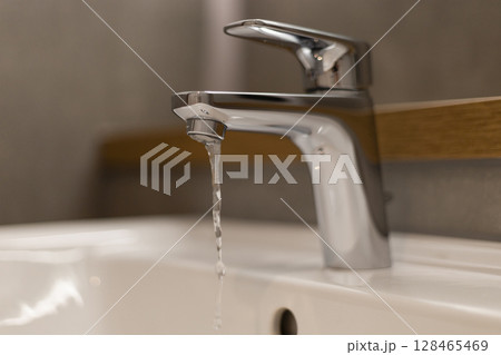 Modern faucet releases a steady stream of water into a clean white sink, showcasing elegant design in a stylish bathroom environment, with a soothing aesthetic 128465469