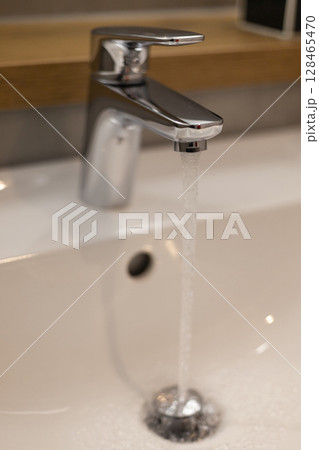 A sleek chrome faucet dispenses a steady stream of water into a pristine white sink, showcasing modern bathroom design with a minimalist aesthetic and clean lines 128465470