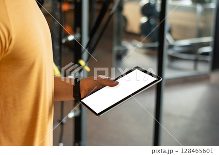 Personal trainer or bodybuilder holding tablet or clipboard in gym or fitness center with white empty screen. Workout plan. Coach making exercise plan. 128465601