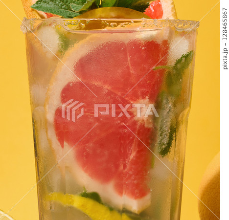 Top of clear glass with cold drink, grapefruit slices, ice and mint on yellow background 128465867