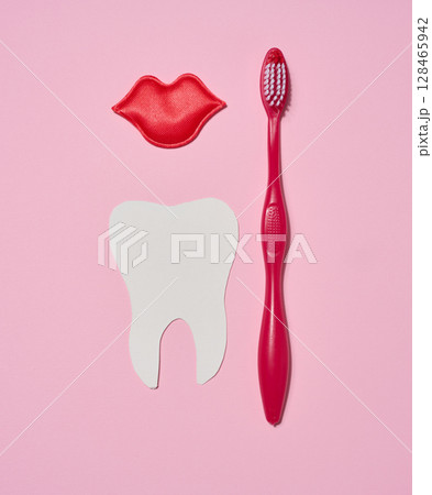 Red toothbrush, red decorative lips and paper cutout white tooth placed on pink background. 128465942