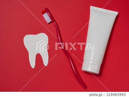 Red toothbrush, white tube of toothpaste and white paper tooth cut out on red background. Red toothbrush, white tube of toothpaste and white paper tooth cut out on red background. 128465943