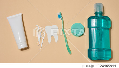 Oral hygiene set including a tube of toothpaste, a toothbrush, dental floss and a bottle of mouthwash, beige background. Top view. Oral hygiene set including a tube of toothpaste, a toothbrush, dental floss and a bottle of mouthwash, beige background. Top view. 128465944