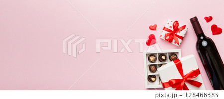 Bottle of red wine on colored background for Valentine Day with gift and chocolate. Heart shaped with gift box of chocolates top view with copy space Bottle of red wine on colored background for Valentine Day with gift and chocolate. Heart shaped with gift box of chocolates top view with copy space 128466385