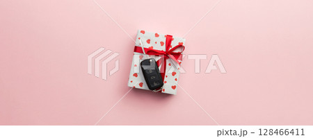 Give gift car key concept top view. Present box with red ribbon bow, heart and car key on pink colored background 128466411