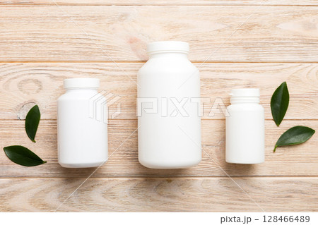 supplement pills with medicine bottle health care and medical top view. Vitamin tablets. Top view mockup bottle for pills and vitamins with green leaves, natural organic bio supplement, copy space 128466489