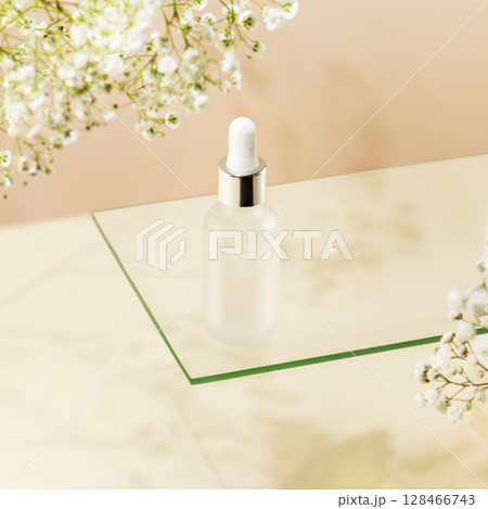 Moisturizing serum. Glass dropper bottle with natural serum on glass shelf on light biege background with white flowers. Organic beauty product and skin friendly cosmetics concept. Mockup 128466743