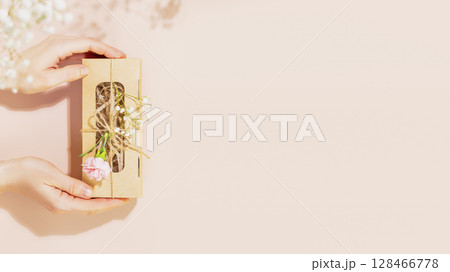 Female hands holding craft gift box with tender flowers on pink background. Romantic holiday background for website. Packaging and delivery concept. Pastel gamma. Flat lay, copy space Female hands holding craft gift box with tender flowers on pink background. Romantic holiday background for website. Packaging and delivery concept. Pastel gamma. Flat lay, copy space 128466778