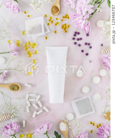 Self care composition with white cosmetic tube with natural cream, herbal tea bags, organic vitamins and supplements with flowers. Organic beauty products and beauty care and treatment concept. Mockup 128466787