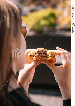 Woman enjoying a freshly baked cookie while seated outdoors in a sunny location Woman enjoying a freshly baked cookie while seated outdoors in a sunny location 128468096